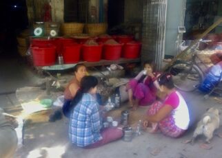 nelja naista istuu kadunvieressa ja syo lounasta Mandalayn kaupungin vilinassa