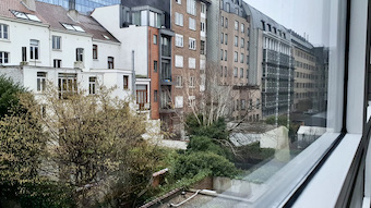 Brysselin asunnon ikkunan takana valkoisia ja punaisia kerrostaloja.