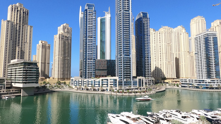 Dubai Marinan lahden korkeat rakennukset ja upeat huviveneet laiturissa sinisen taivaan alla.