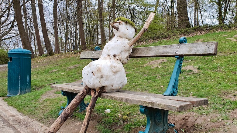 Puujalkainen lumiukko istuu puisella puiston penkilla.