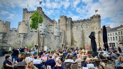 Gravensteen linna ja edustalla iloisia lomalaisia istumassa ulkoravintolassa.