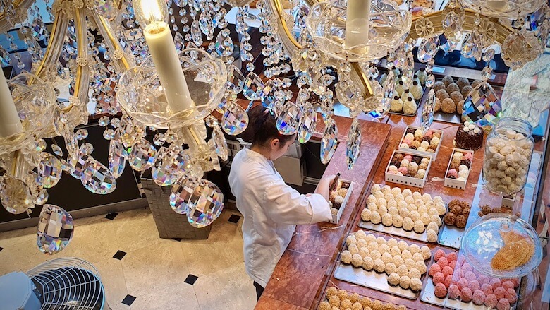 Kristallikruunun alapuolella nainen pakkaa leivoksia laatikkoon leipomokahvilassa Bruggessa.