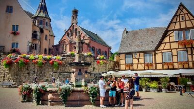 Tori ja turisteja ihailemassa Eguisheimin ristikkorakenteisia taloja torilla.