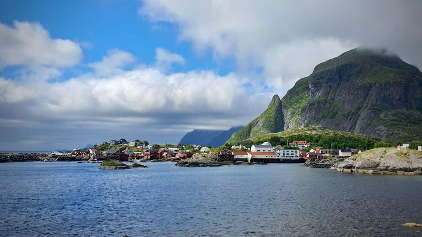 Ison vuoren juurella punaisia taloja ja etualalla meri, Å i Lofoten.