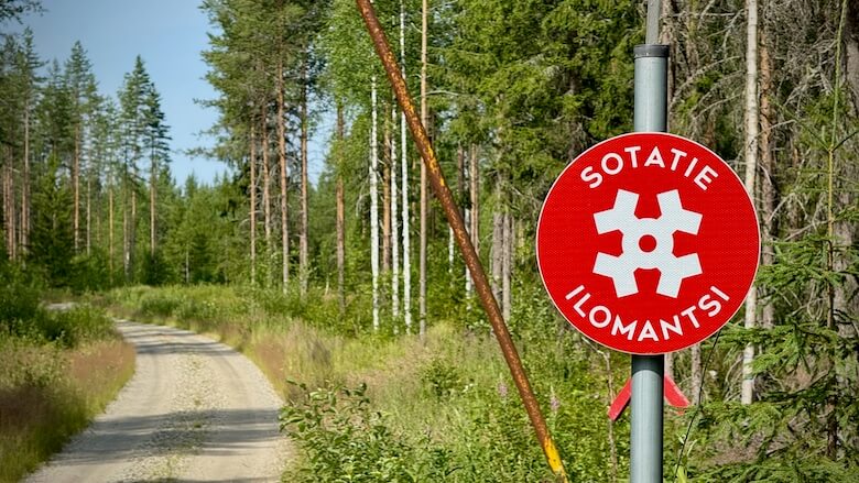 Punainen sotatie liikennemerkki kapean tien reunassa.