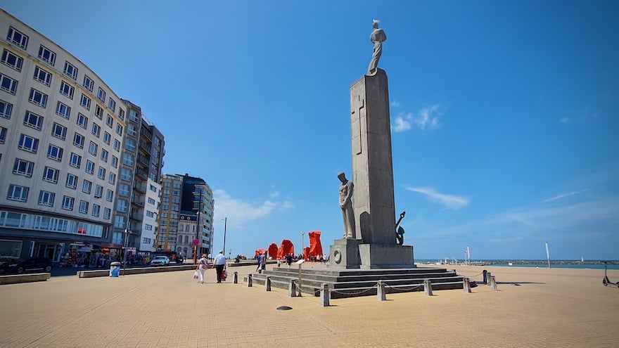 Patsas aukiolla ja meri ja kerrostaloja patsaan toisella puolella.